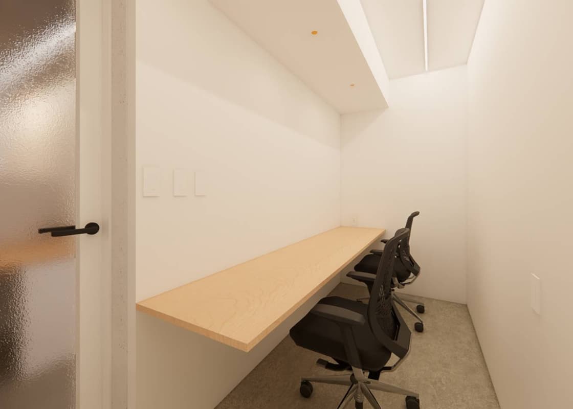 白い壁に囲まれた小さな個室、木製のカウンターデスクと2つの黒いオフィスチェア